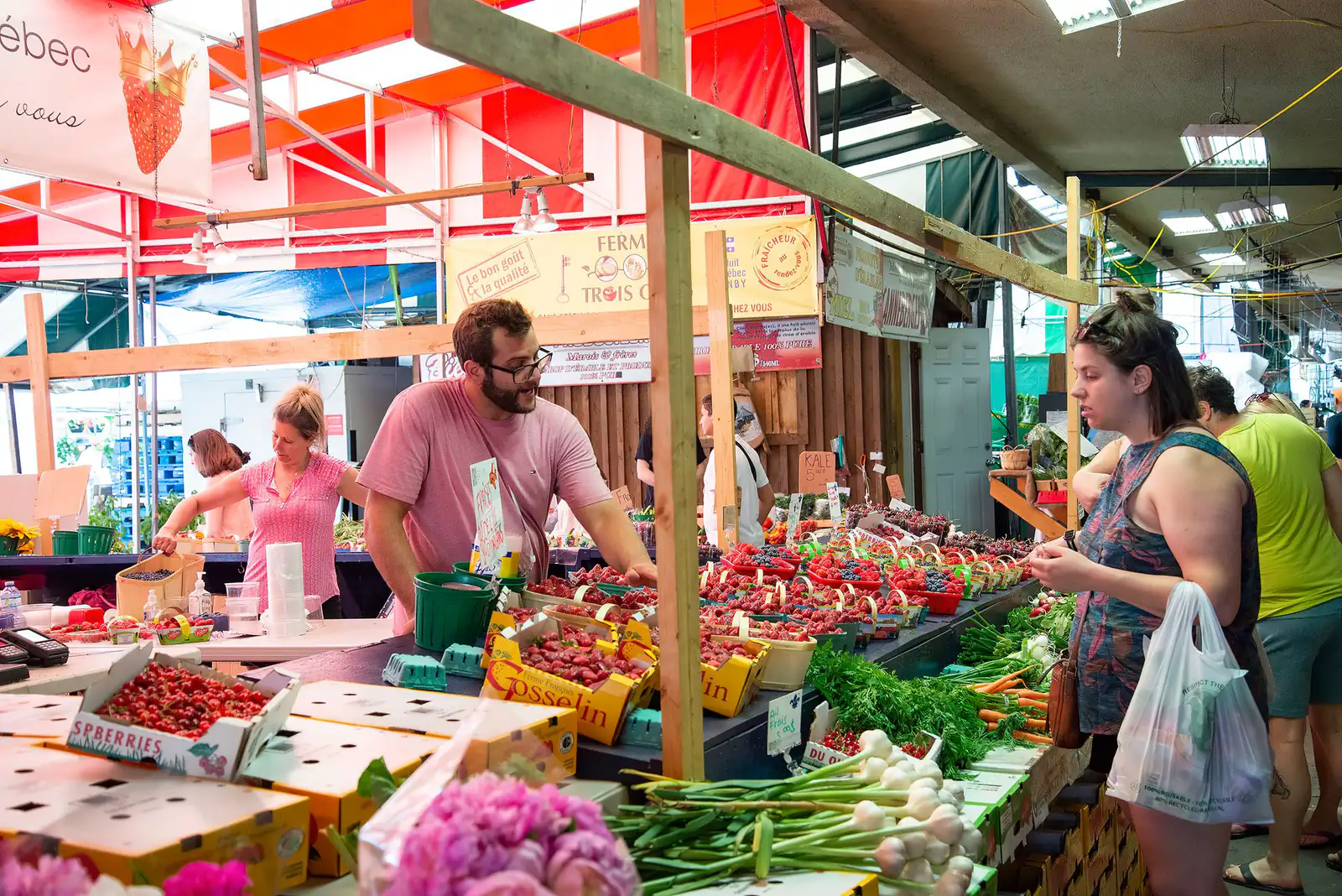 Shoppers browsing fresh produce and flowers at a busy covered market stall in Canada