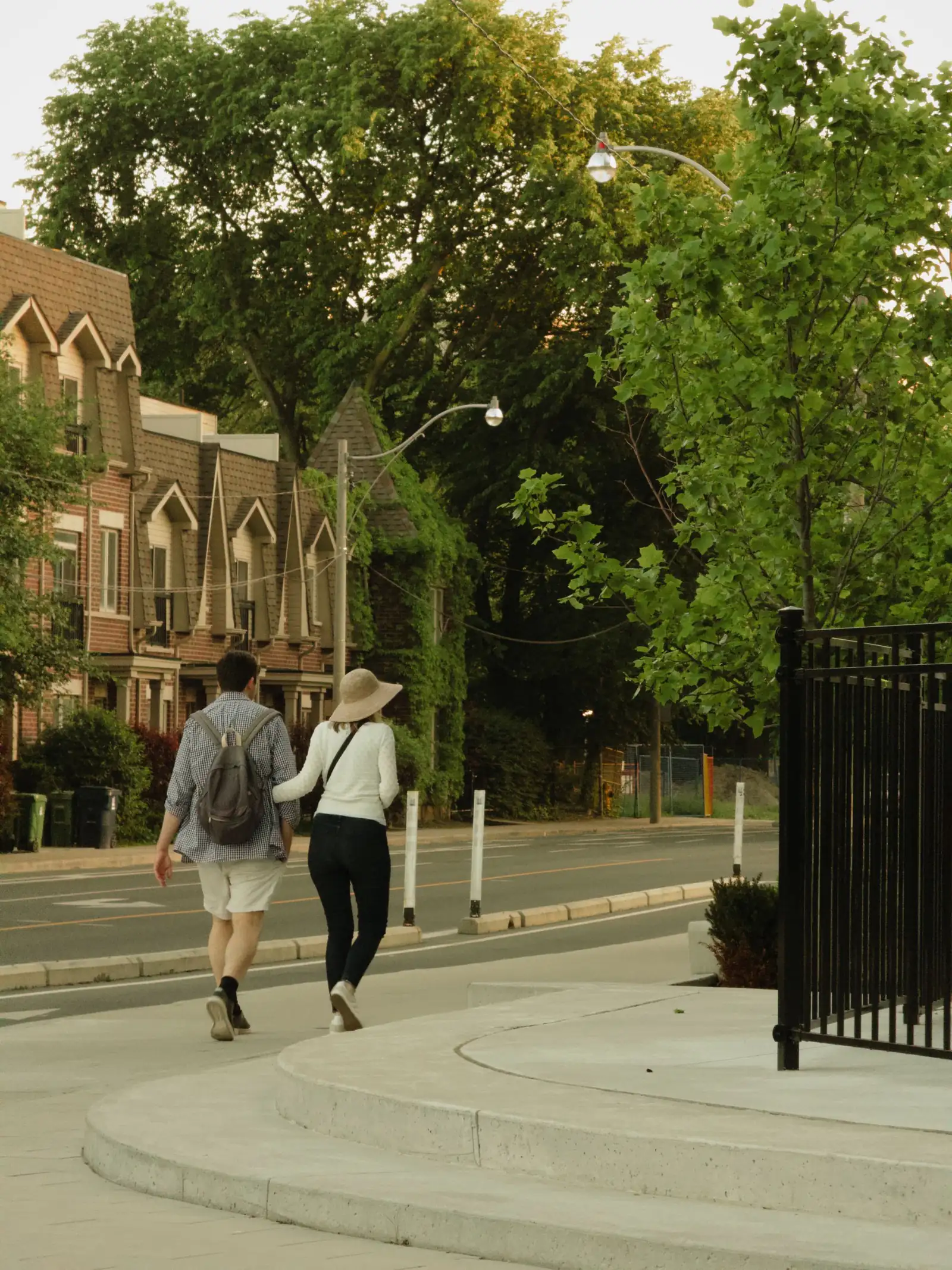 A couple walking along a leafy residential street lined with brick row houses in Toronto